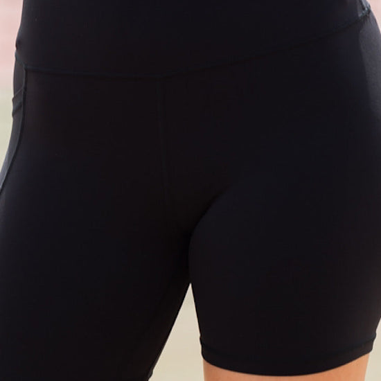 Women wearing black high-waisted shorts with phone pockets and an orange high coverage sports bra.