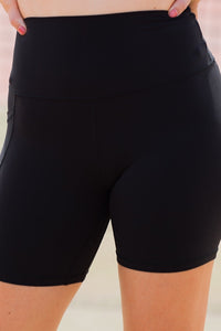 Women wearing black high-waisted shorts with phone pockets and an orange high coverage sports bra.