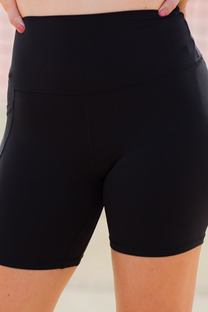 Women wearing black high-waisted shorts with phone pockets and an orange high coverage sports bra.