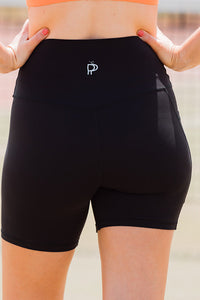 Women wearing black high-waisted shorts with phone pockets and an orange high coverage sports bra.