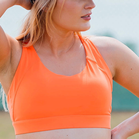 Women wearing orange sports bra and black phone pocket shorts.