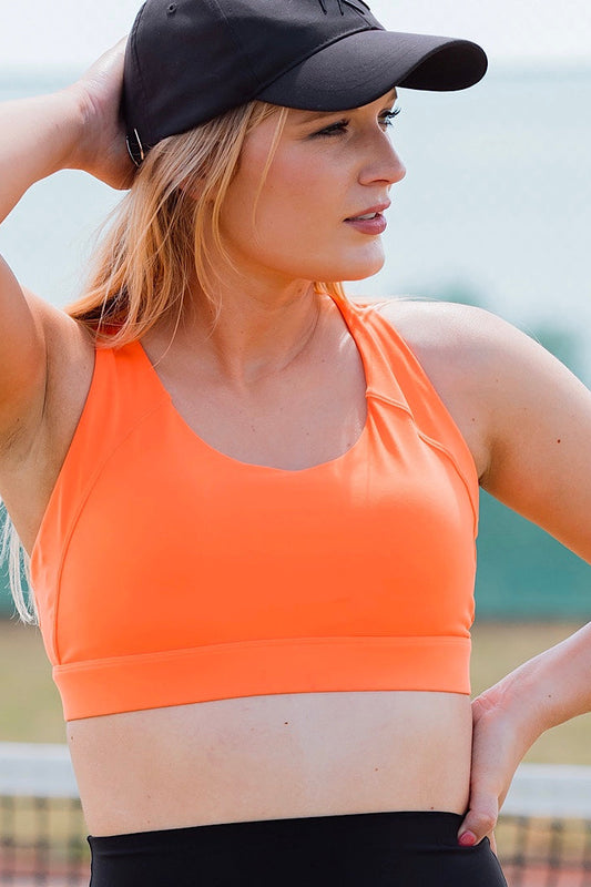 Women wearing orange sports bra and black phone pocket shorts.