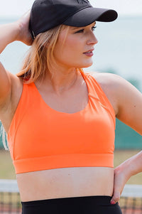 Women wearing orange sports bra and black phone pocket shorts.