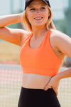 Women wearing orange sports bra and black phone pocket shorts.