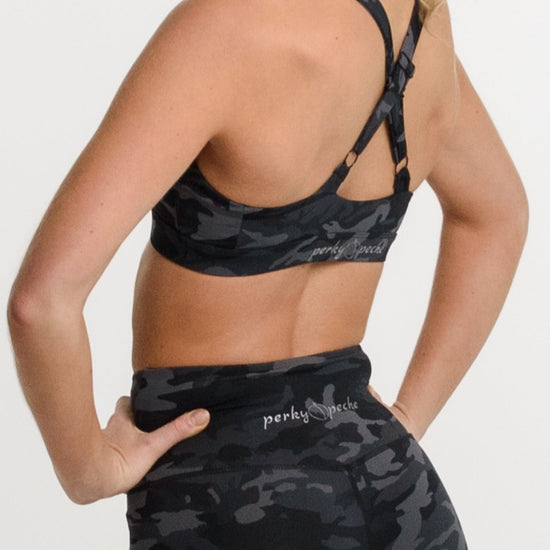 A woman shown from the back wearing a matching black and gray camouflage activewear set, featuring a sports bra and high-waisted biker shorts, against a plain white studio background.