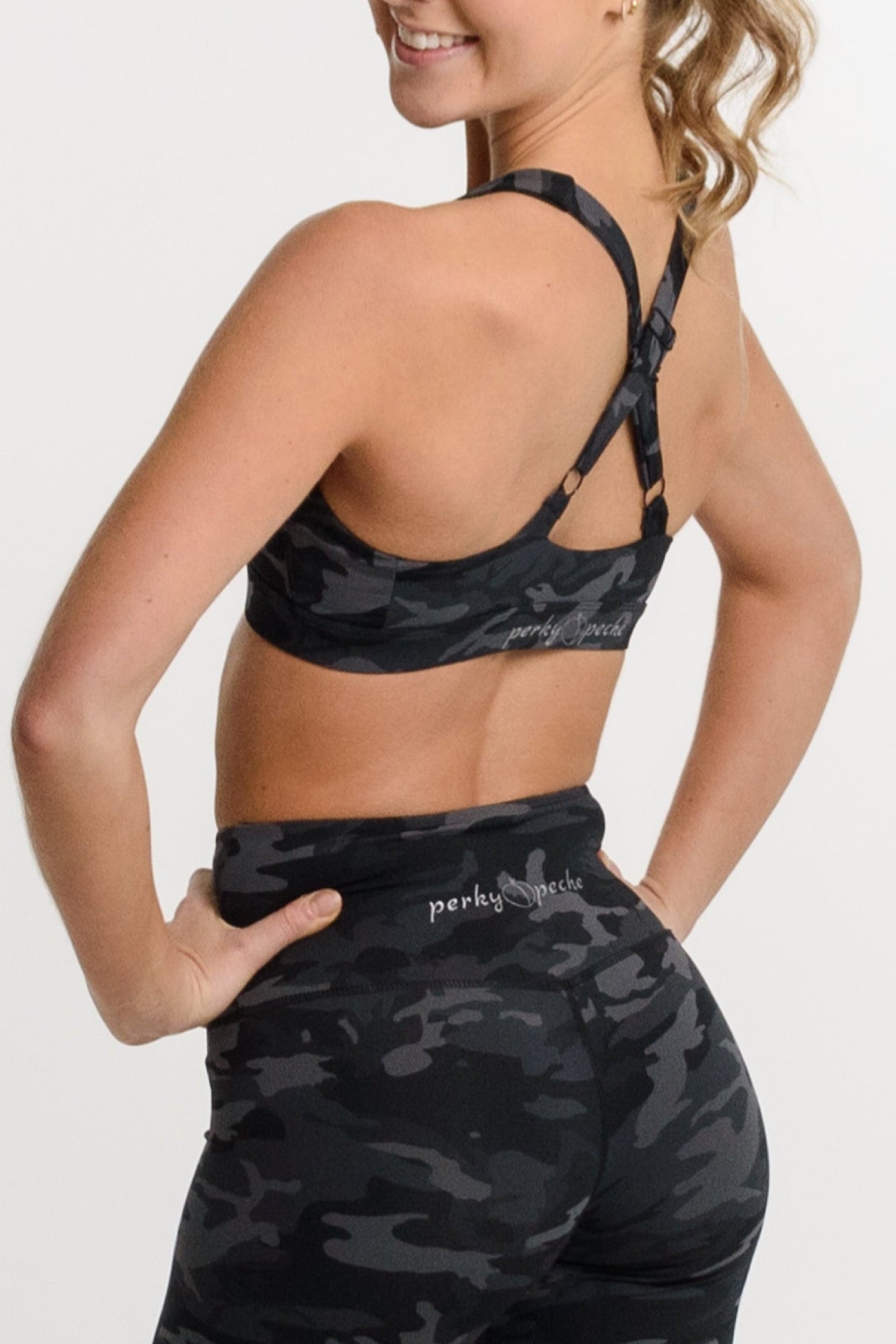 A woman shown from the back wearing a matching black and gray camouflage activewear set, featuring a sports bra and high-waisted biker shorts, against a plain white studio background.