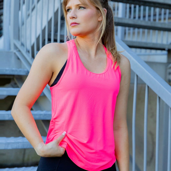 Woman wearing a bright pink tank top and black phone pocket leggings