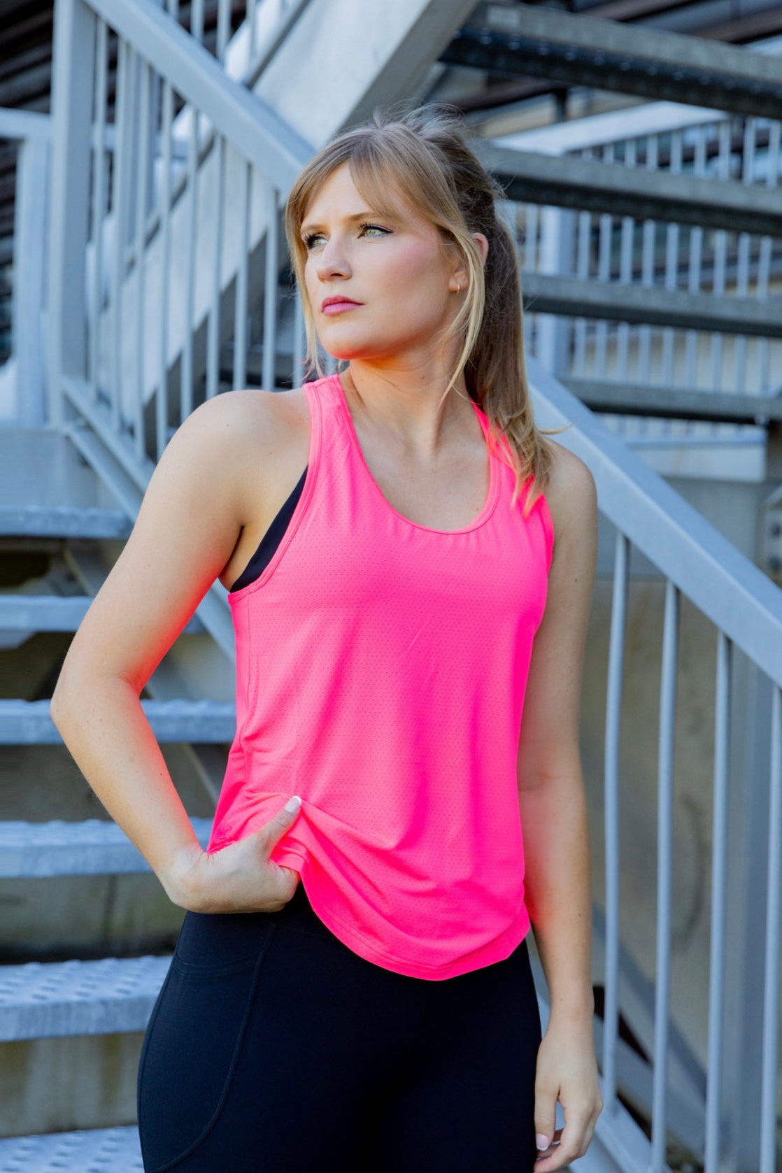 Woman wearing a bright pink tank top and black phone pocket leggings