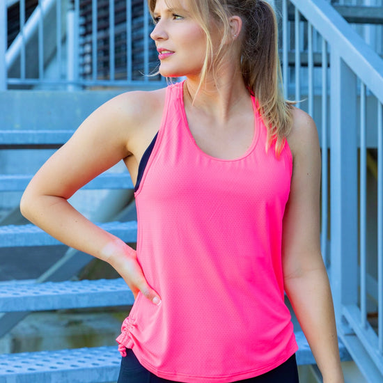 Woman wearing a bright pink tank top and black phone pocket leggings