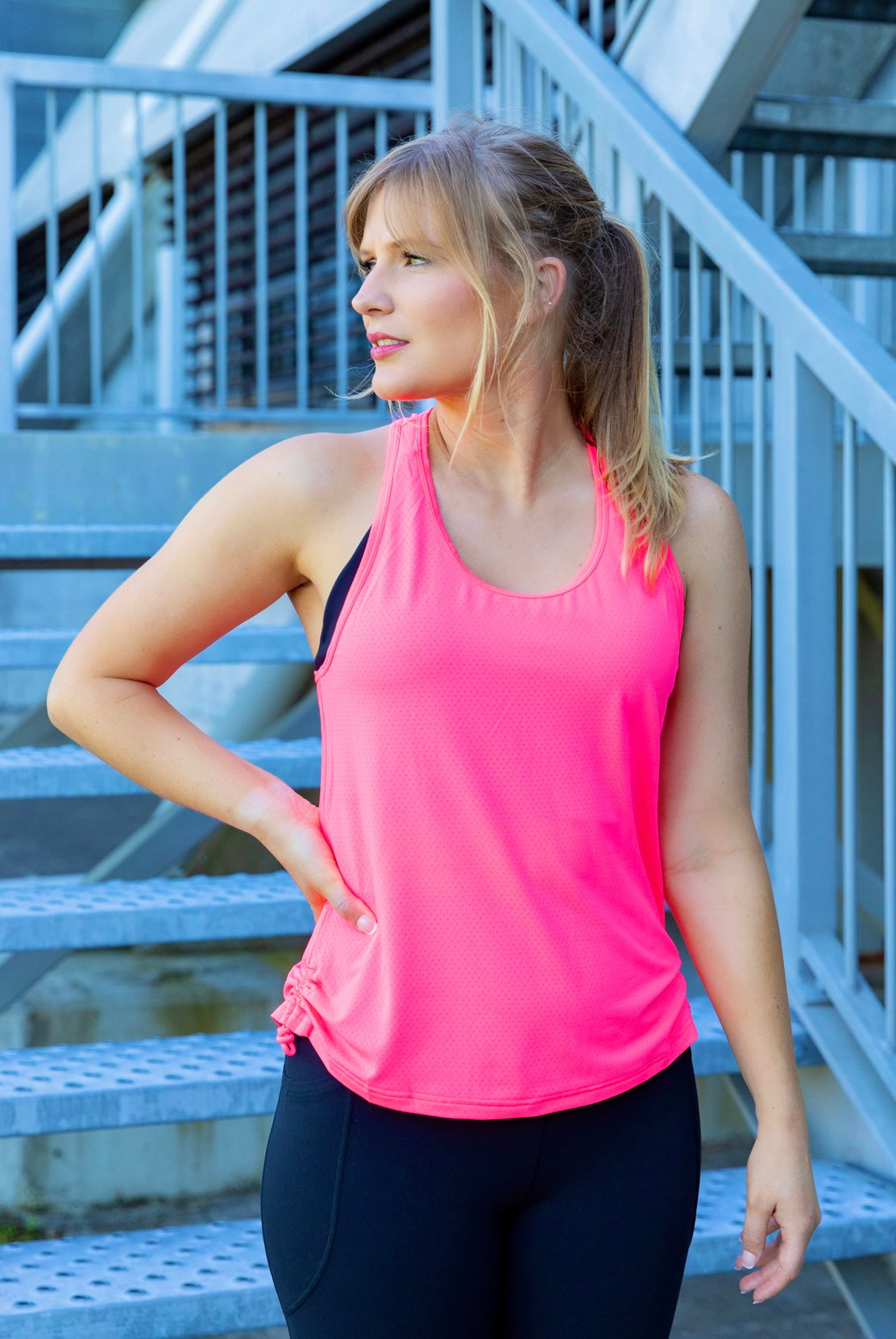 Woman wearing a bright pink tank top and black phone pocket leggings