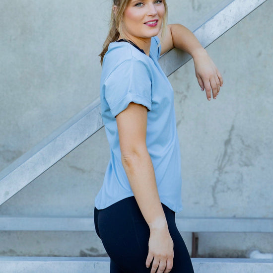Woman wearing a scoop neck light blue t-shirt with rolled sleeves and black high waisted leggings