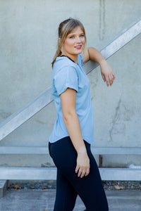 Woman wearing a scoop neck light blue t-shirt with rolled sleeves and black high waisted leggings