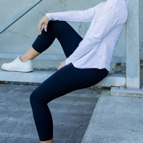 Woman sitting on a concrete step wearing a white long-sleeve top and black leggings.