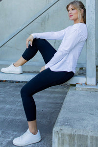 Woman sitting on a concrete step wearing a white long-sleeve top and black leggings.