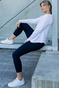 Woman sitting on a concrete step wearing a white long-sleeve top and black leggings.
