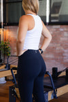 women wearing a white tank top and black leggings in a Pilates reformer room.