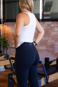 women wearing a white tank top and black leggings in a Pilates reformer room.