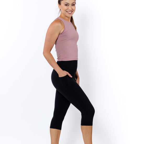 Woman wearing a sleeveless top and black 3/4 high-waisted leggings with phone pockets