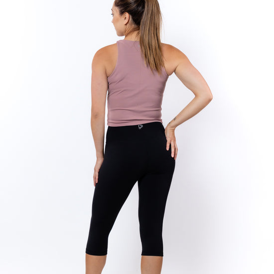 Woman wearing a pink tank top and black capri leggings