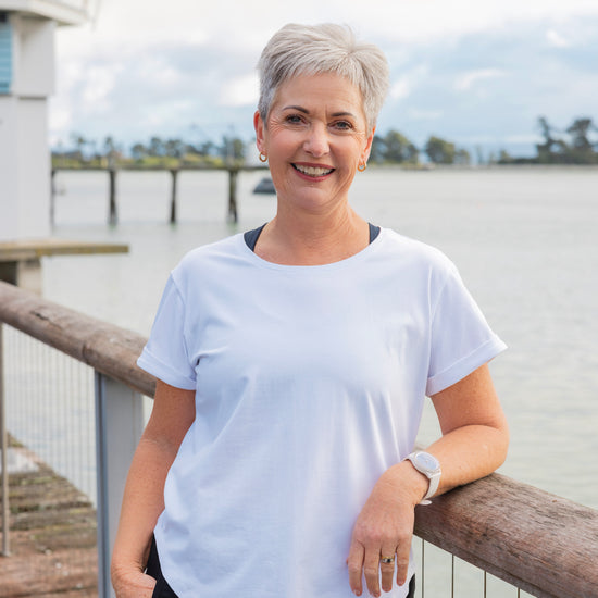 Woman in a white t-shirt standing on a wooden deck by a waterfront.