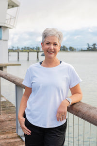 Woman in a white t-shirt standing on a wooden deck by a waterfront.