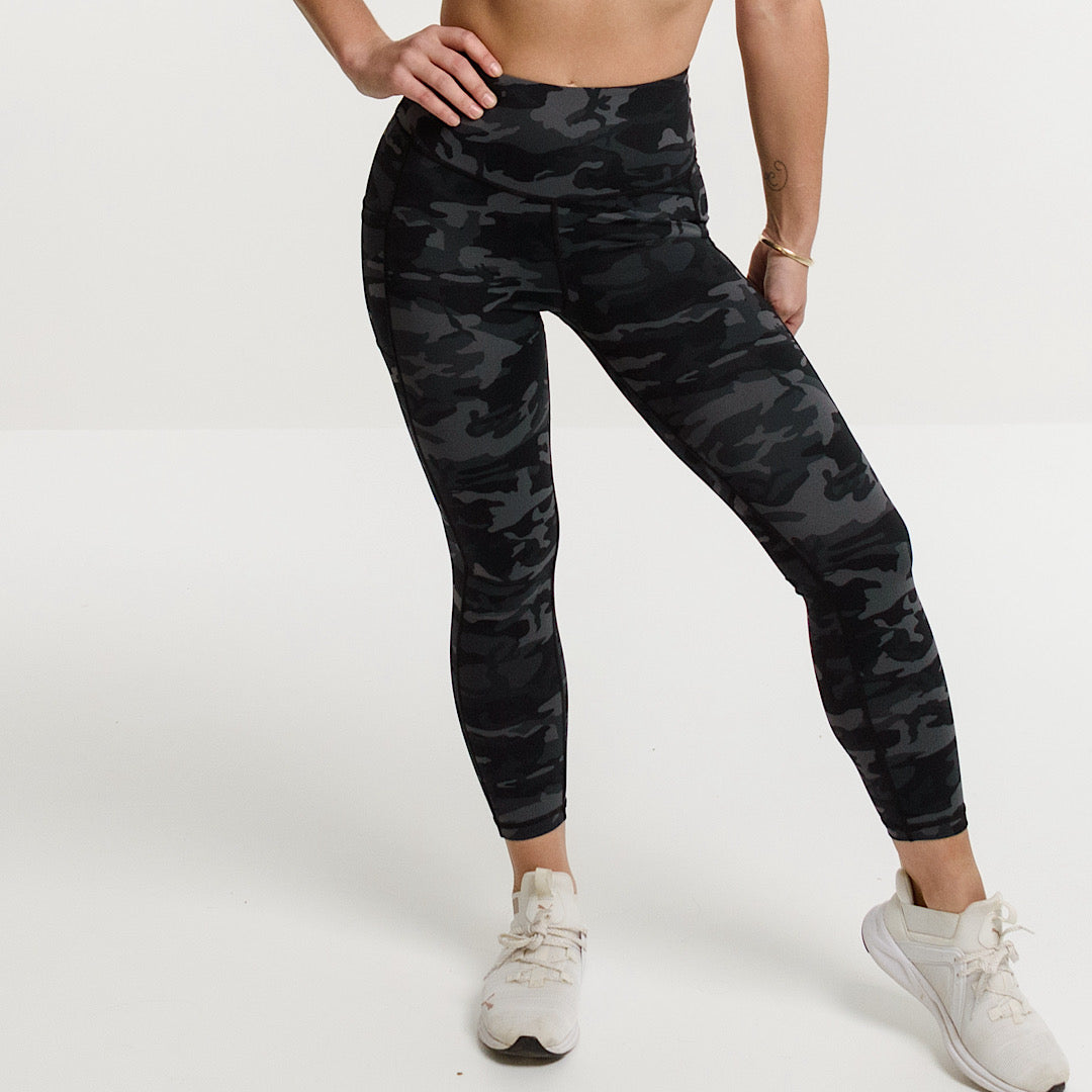 Woman in black sports bra and camouflage pocket leggings.