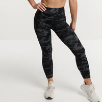 Woman in black sports bra and camouflage pocket leggings.