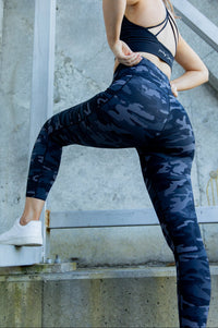 Woman in black sports bra and camouflage pocket leggings.