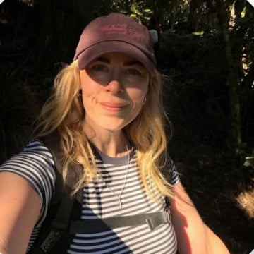 A woman outdoors wearing a striped shirt and a pink cap, with a blue 'Follow' button below on a blurred gradient background.