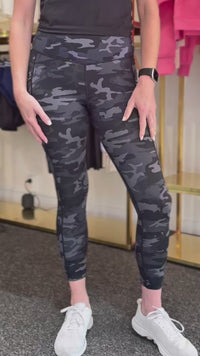 Woman in black sports top and camouflage pocket leggings.